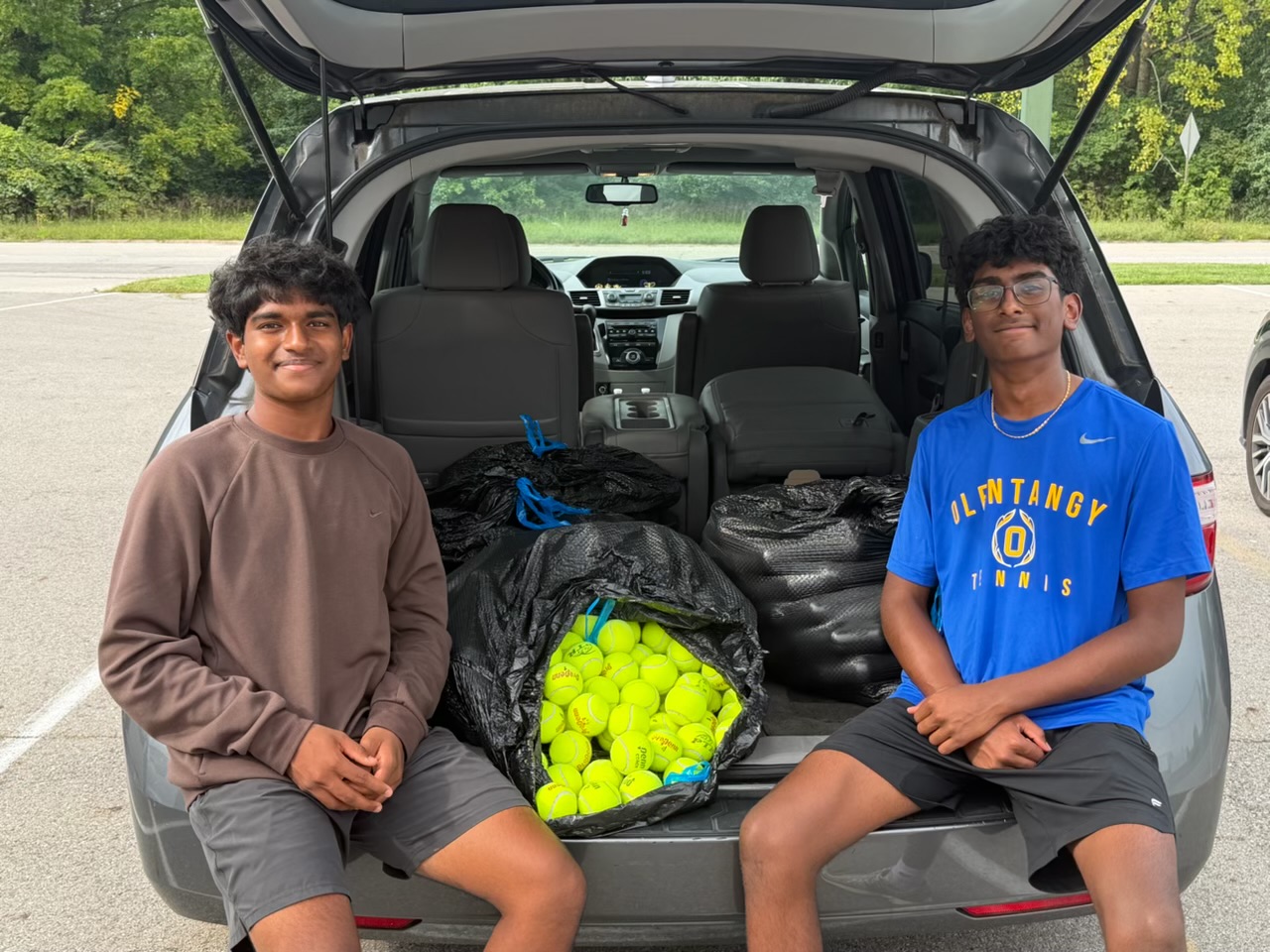 Prathik Amathi and Jashwin Pisini sitting in the trunk of a car packed with bags of donated tennis balls