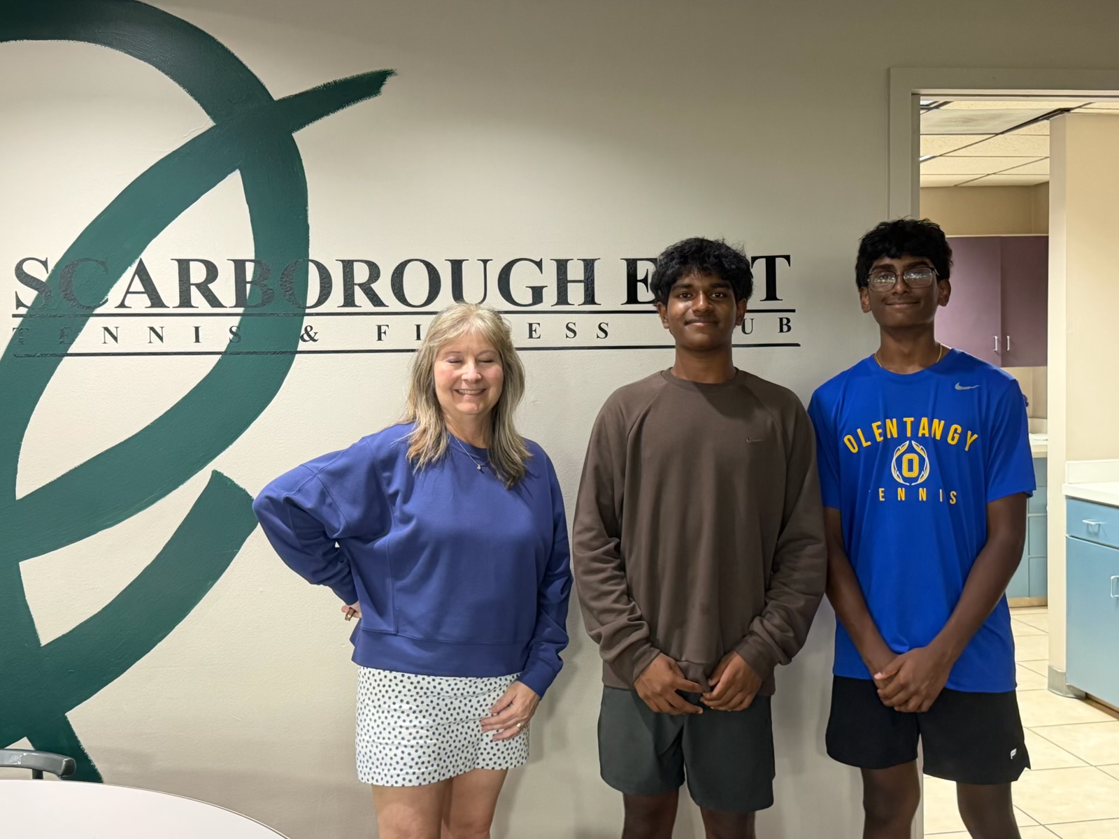 Jacqueline Boggs of Scarborough East standing with Prathik Amathi and Jashwin Pisini in front of the Scarborough East Tennis and Fitness Club sign